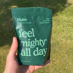 Hand holding a green package of Mighty Mushroom Gummies against a grassy background.